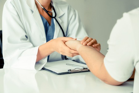 112064014-woman-doctor-talks-to-female-patient-in-hospital-office-while-examining-the-patients-pulse-by-hands